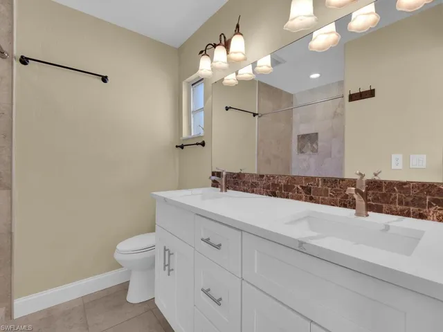Bathroom with a tile shower, a sink, toilet, and tile patterned floors
