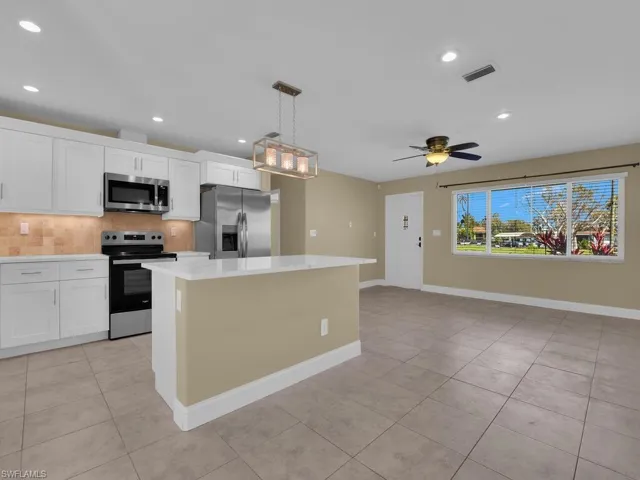 Kitchen featuring light countertops, a kitchen island, stainless steel appliances, visible vents, and decorative backsplash