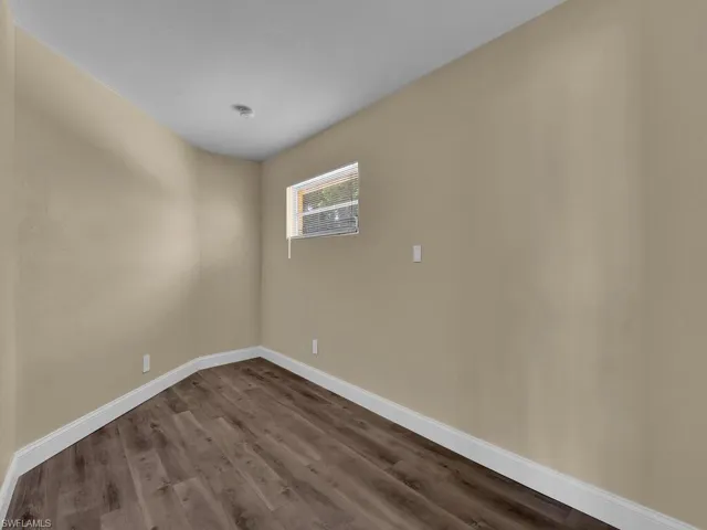 Unfurnished room featuring baseboards and dark wood-style floors