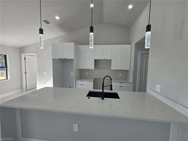 Kitchen featuring pendant lighting, white cabinetry, lofted ceiling, and sink