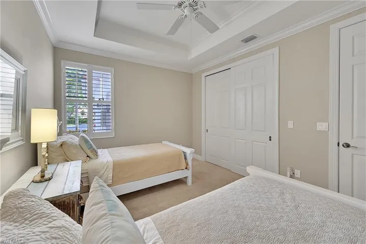 Carpeted bedroom featuring a closet, a raised ceiling, ornamental molding, and ceiling fan