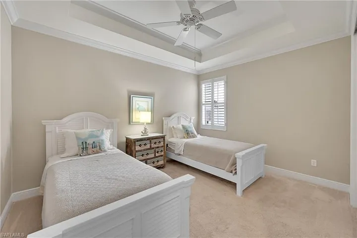 Bedroom with a raised ceiling, light carpet, ornamental molding, baseboards, and ceiling fan