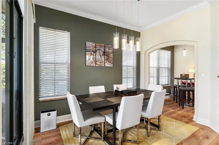 Dining space featuring arched walkways, baseboards, crown molding, and wood finished floors