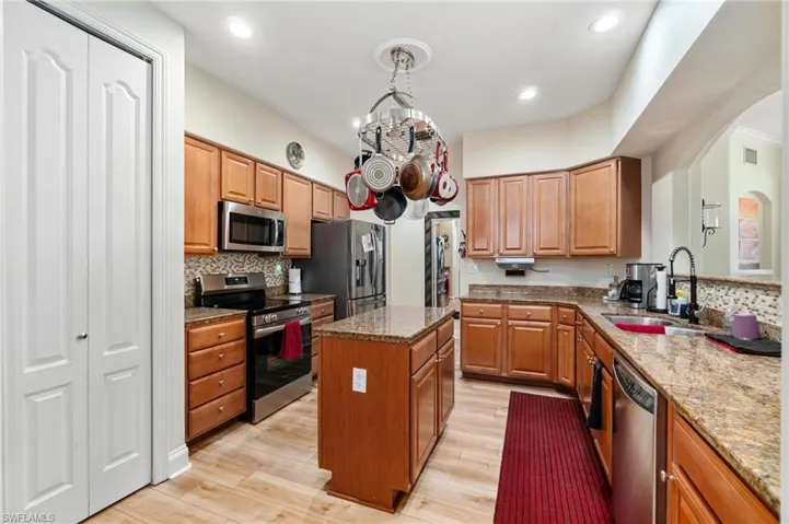 Kitchen featuring stainless steel appliances, a sink, arched walkways, light wood-style floors, and a kitchen island