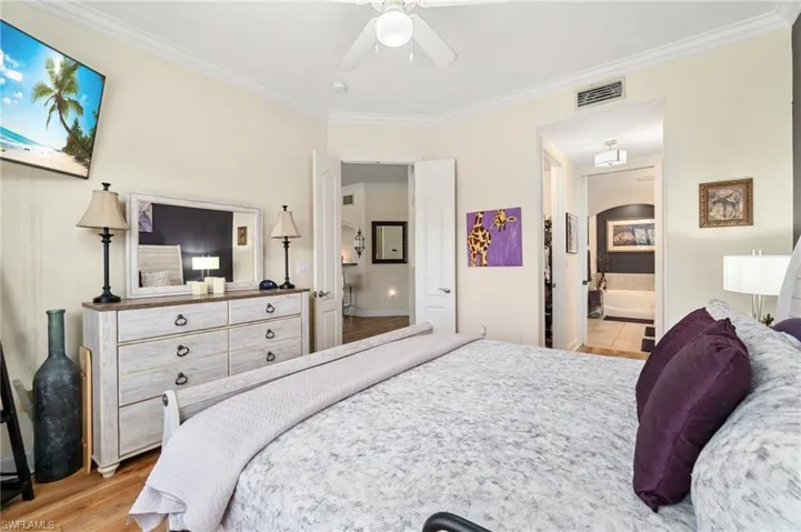 Bedroom with light wood-style flooring, ensuite bathroom, visible vents, ceiling fan, and crown molding
