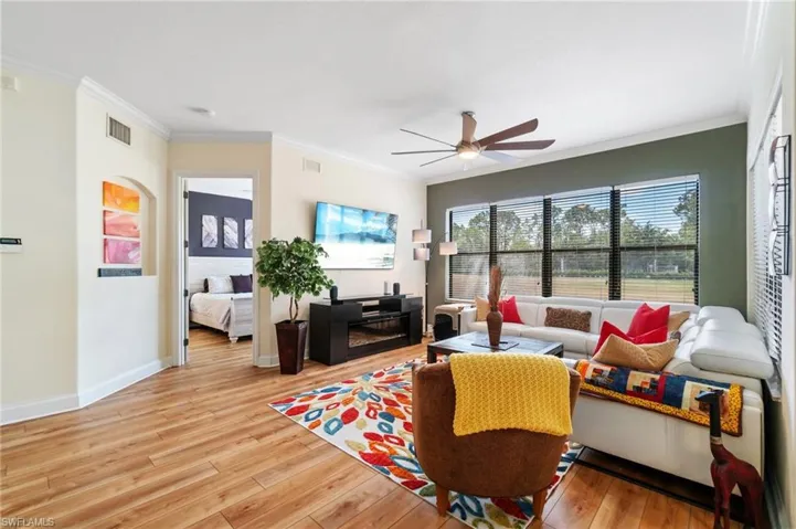 Living area with visible vents, a ceiling fan, ornamental molding, baseboards, and light wood-style flooring