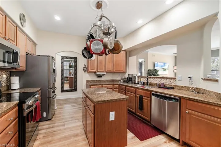 Kitchen with a sink, arched walkways, light wood-style floors, a kitchen island, and appliances with stainless steel finishes