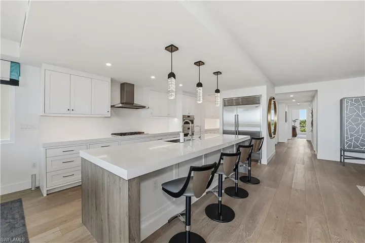 Kitchen featuring a breakfast bar area, light wood-type flooring, a center island with sink, white cabinets, and hanging light fixtures