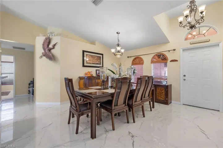 Vaulted ceiling dining area featuring marble-look tile flooring, a multi-paneled entry door with an arched transom, and two arched windows with wood blinds