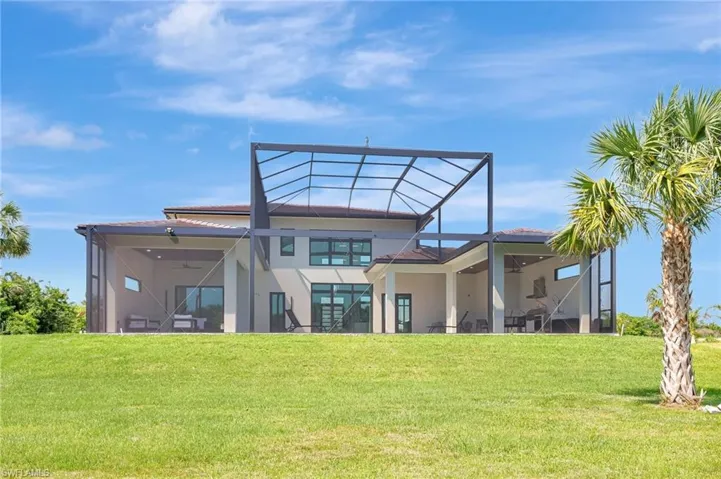 Rear view of property featuring stucco siding, a ceiling fan, glass enclosure, and a lawn