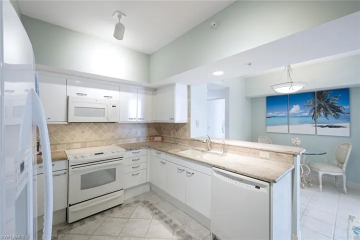 Kitchen with a sink, white appliances, a peninsula, white cabinetry, and tasteful backsplash