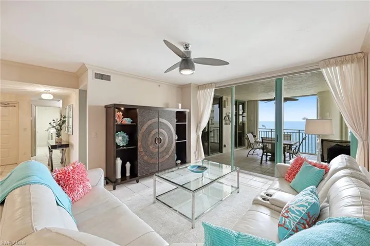 Living area with ceiling fan, a wall of windows, a water view, visible vents, and ornamental molding