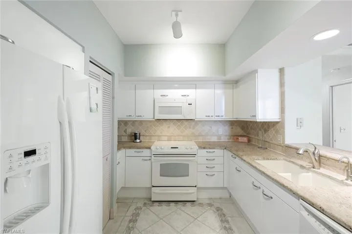 Kitchen with decorative backsplash, a sink, white cabinets, white appliances, and light tile patterned flooring