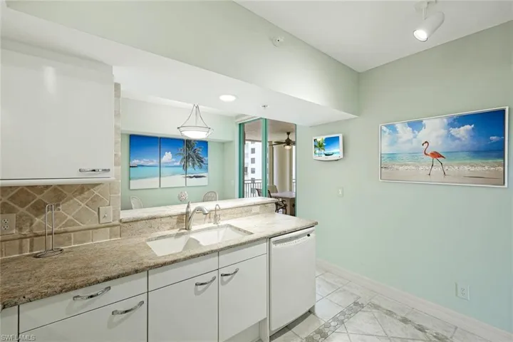 Kitchen featuring light stone countertops, a sink, dishwasher, white cabinetry, and baseboards