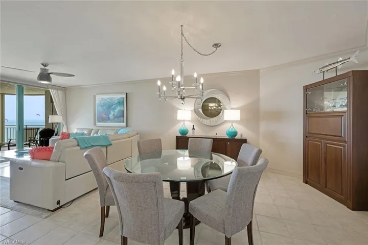 Dining room with light tile patterned floors, baseboards, ornamental molding, and ceiling fan with notable chandelier