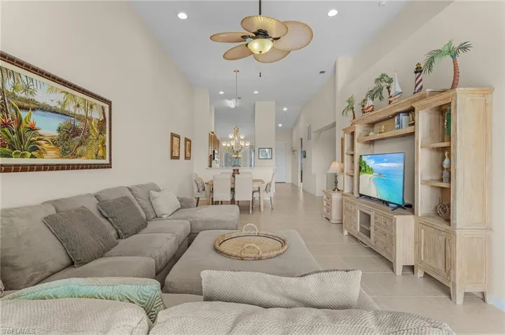 Tiled living room with ceiling fan with notable chandelier and a towering ceiling