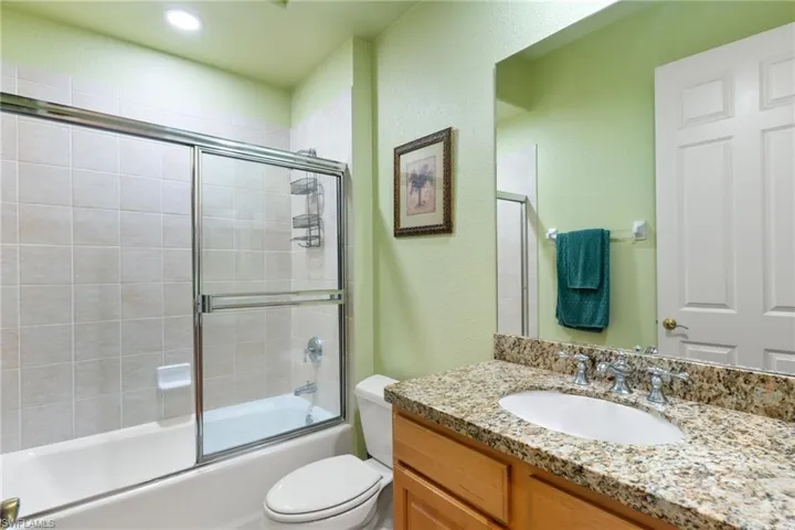 Full bath with shower / bath combination with glass door, vanity, and a textured wall