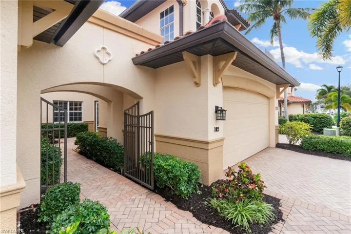 View of exterior entry featuring a garage, a tiled roof, stucco siding, a gate, and decorative driveway