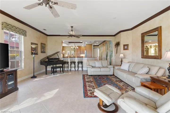 Living room featuring ornamental molding, a ceiling fan, a chandelier, and light tile patterned flooring