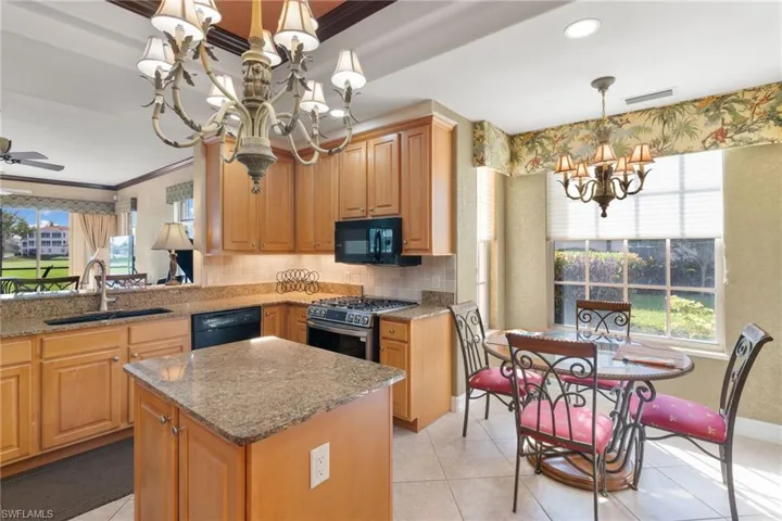 Kitchen with a chandelier, hanging light fixtures, black appliances, light stone countertops, and backsplash
