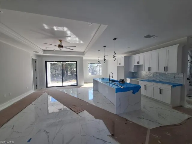 Kitchen featuring decorative backsplash, sink, a tray ceiling, an island with sink, and white cabinets