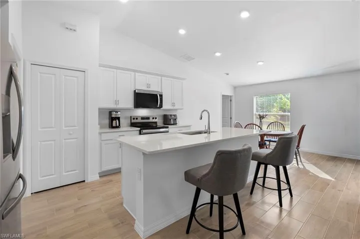 Kitchen with lofted ceiling, white cabinets, a kitchen island with sink, appliances with stainless steel finishes, and a kitchen bar