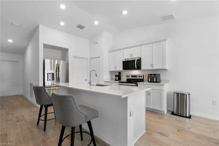 Kitchen with stainless steel appliances, a breakfast bar, a center island with sink, white cabinetry, and light stone countertops