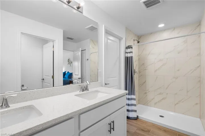 Bathroom featuring double vanity, a stall shower, ensuite bath, wood finish floors, and recessed lighting
