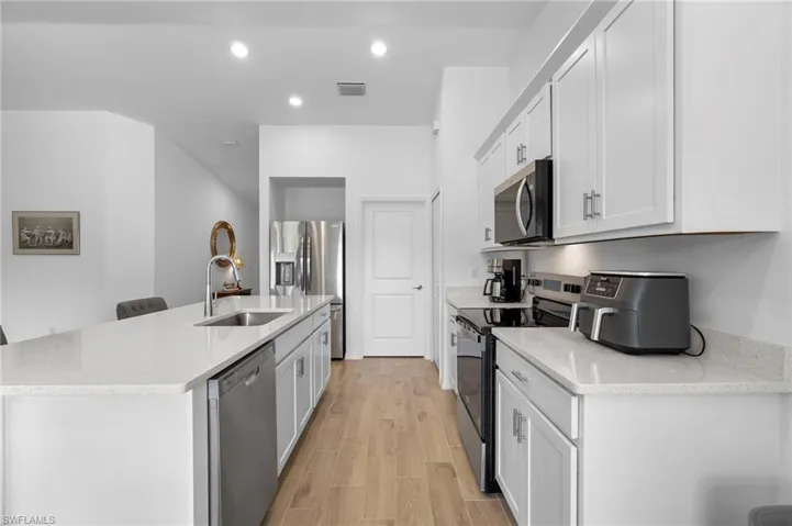 Kitchen with appliances with stainless steel finishes, light stone counters, recessed lighting, a kitchen island with sink, and white cabinets