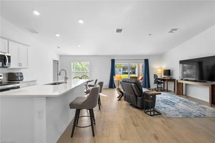 Kitchen featuring a breakfast bar, open floor plan, a kitchen island with sink, stainless steel appliances, and white cabinets
