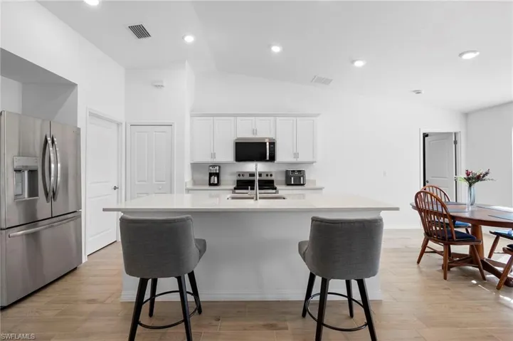 Kitchen featuring stainless steel appliances, vaulted ceiling, a center island with sink, a breakfast bar, and white cabinets