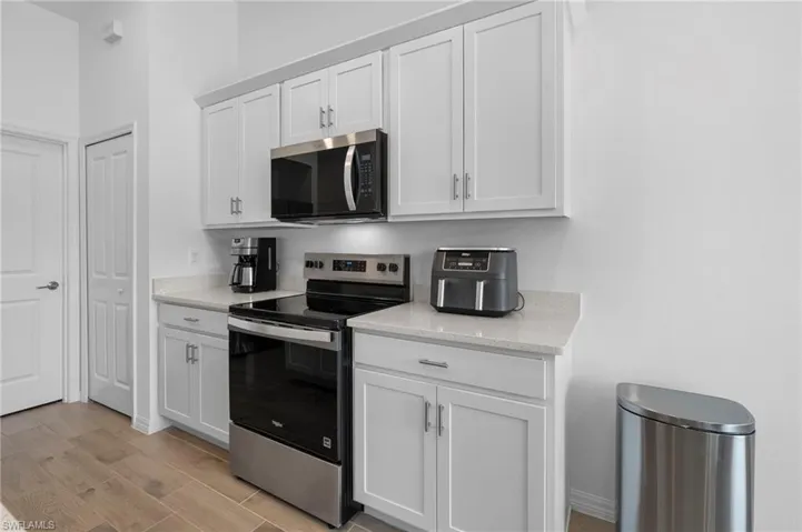 Kitchen with stainless steel appliances, white cabinets, light stone counters, and light wood finished floors