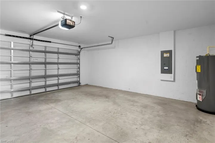 Garage with electric water heater, electric panel, a garage door opener, and concrete block wall
