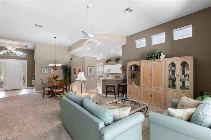 Living room with a high ceiling, ceiling fan with notable chandelier, and light carpet