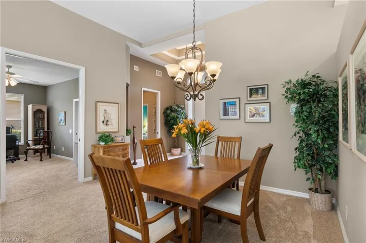 Carpeted dining area with a high ceiling, ceiling fan with notable chandelier, and a tray ceiling
