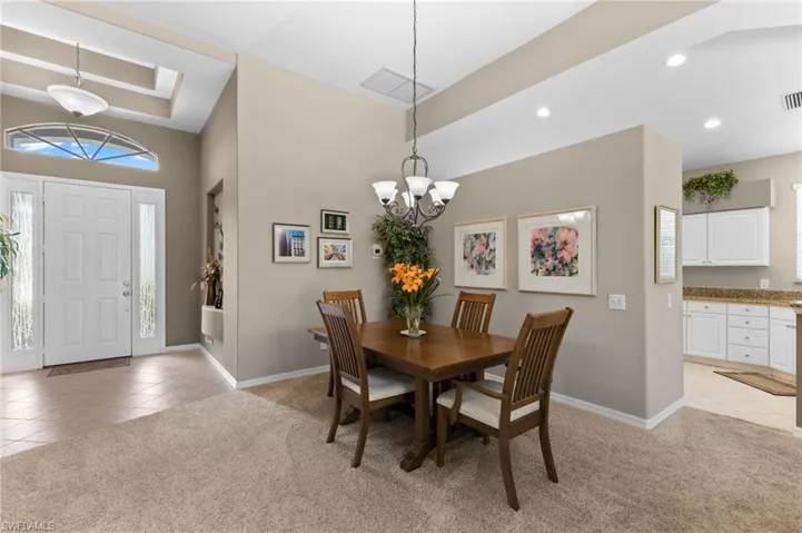 Carpeted dining room featuring a raised ceiling and an inviting chandelier