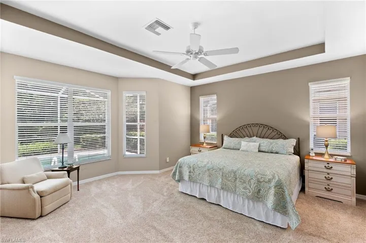 Bedroom featuring ceiling fan, a tray ceiling, and light colored carpet