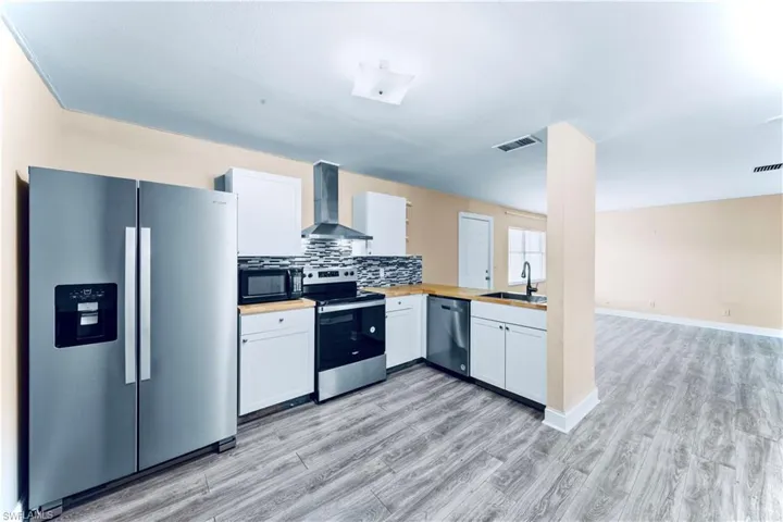 Kitchen with stainless steel appliances, wall chimney exhaust hood, light wood-type flooring, and white cabinets
