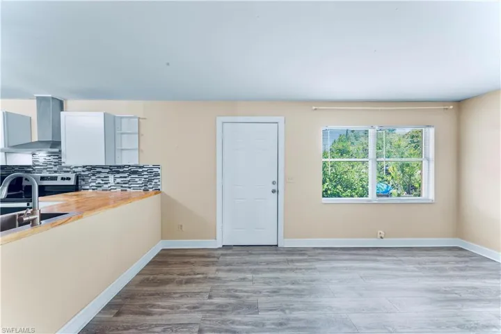 Kitchen featuring wall chimney range hood, backsplash, wood finished floors, stainless steel electric range, and wooden counters