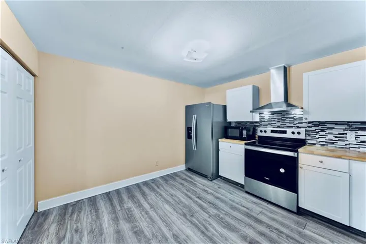 Kitchen with electric range, wall chimney exhaust hood, refrigerator with ice dispenser, black microwave, and light wood-type flooring