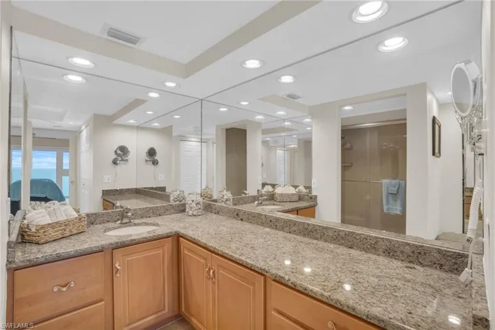 Dual sink vanity featuring light wood-finish cabinetry and stone countertops