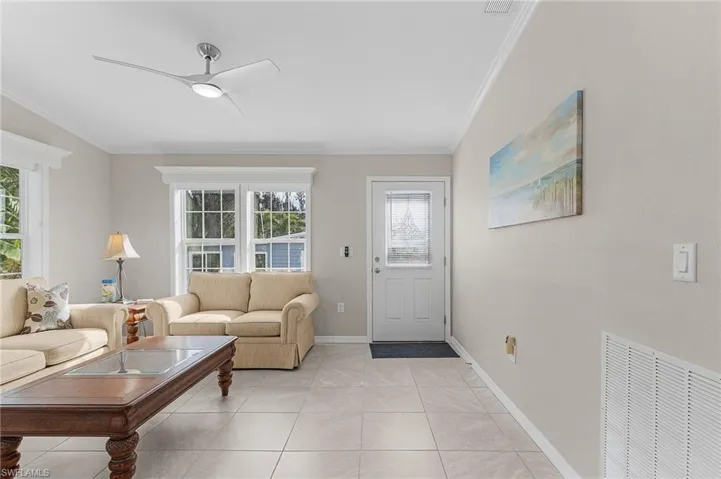 Living room with ceiling fan, light tile floors, and crown molding