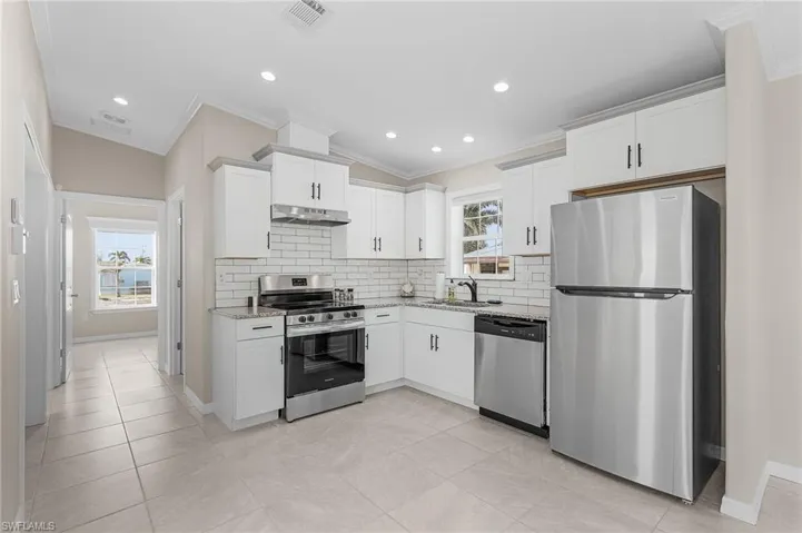 Kitchen with granite countertops, white cabinets, stainless steel appliances, sink, and plenty of natural light