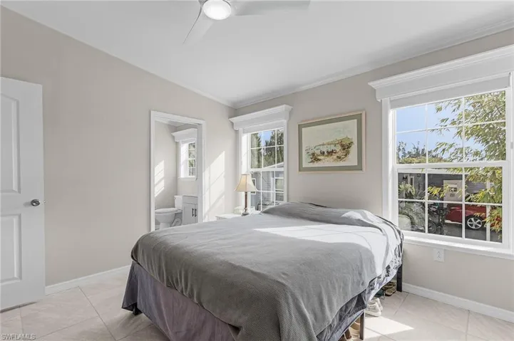 Tiled bedroom featuring vaulted ceiling, ceiling fan, ensuite bathroom, and crown molding