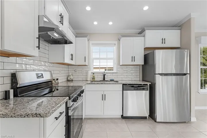 Kitchen with sink, granite countertops, stainless steel appliances, ornamental molding, and white cabinets