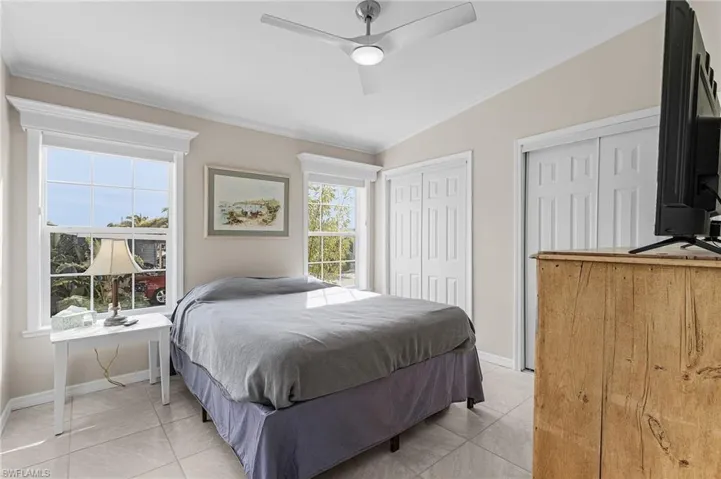 Bedroom with ceiling fan, two closets, light tile floors, and crown molding