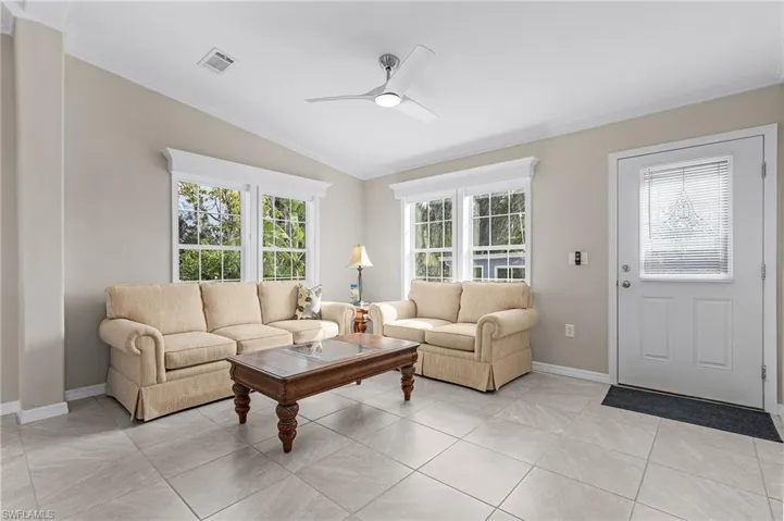 Living room with ceiling fan, light tile floors, vaulted ceiling, and a healthy amount of sunlight