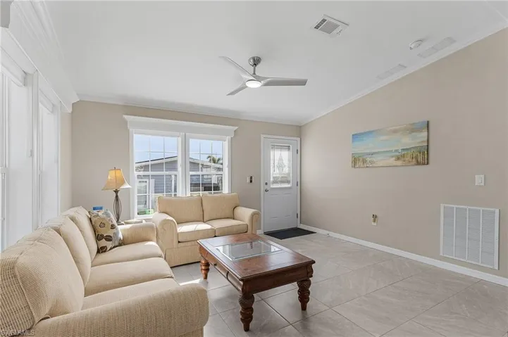 Living room with ceiling fan, ornamental molding, and light tile flooring
