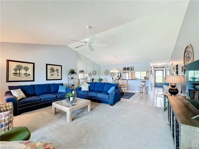 Living room featuring ceiling fan, vaulted ceiling, a textured ceiling, and light carpet