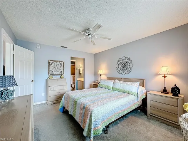 Carpeted bedroom featuring a textured ceiling, ceiling fan, and ensuite bath